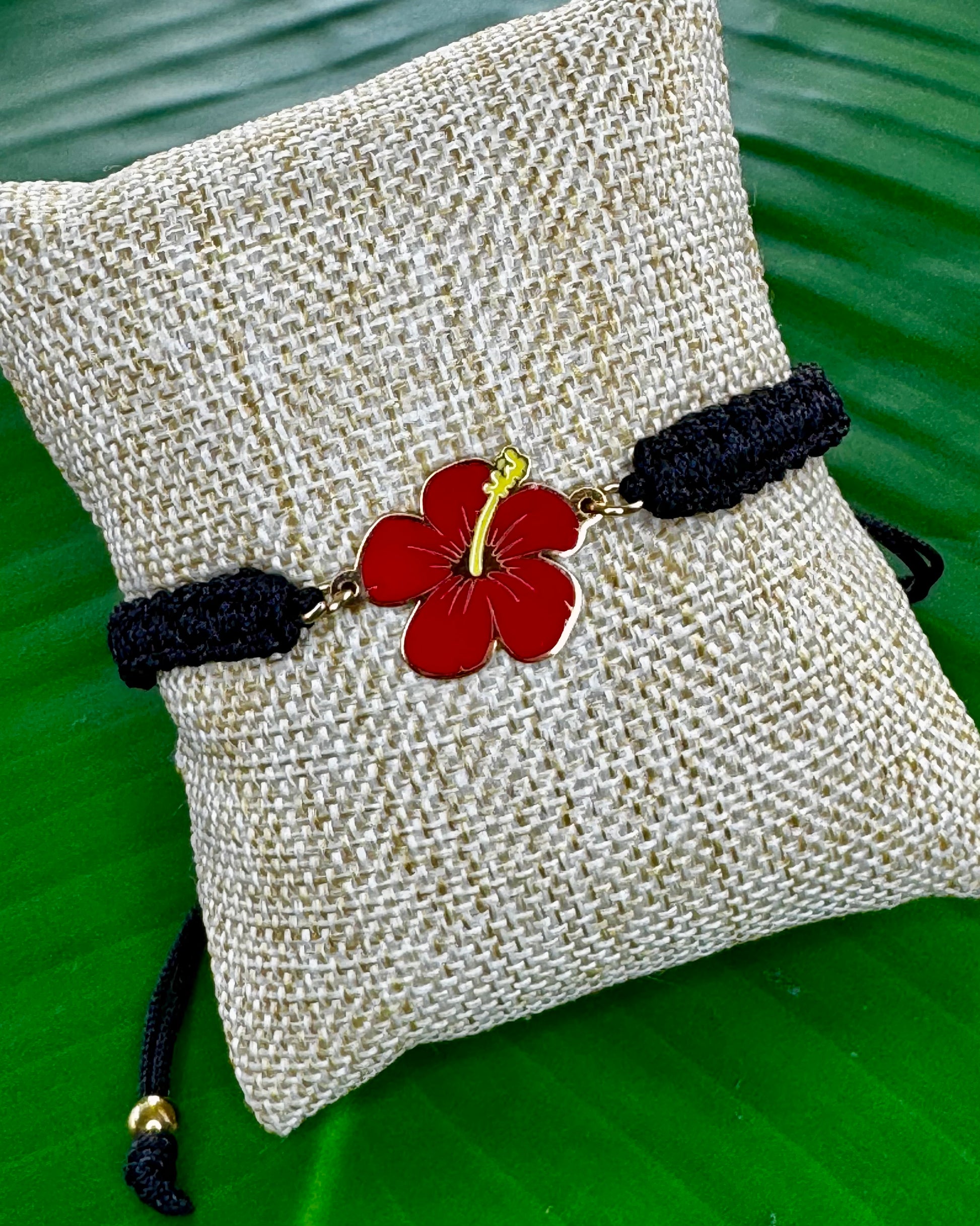 Black adjustable thread bracelet with a gold or silver Flor de Maga charm displayed on a neutral background.