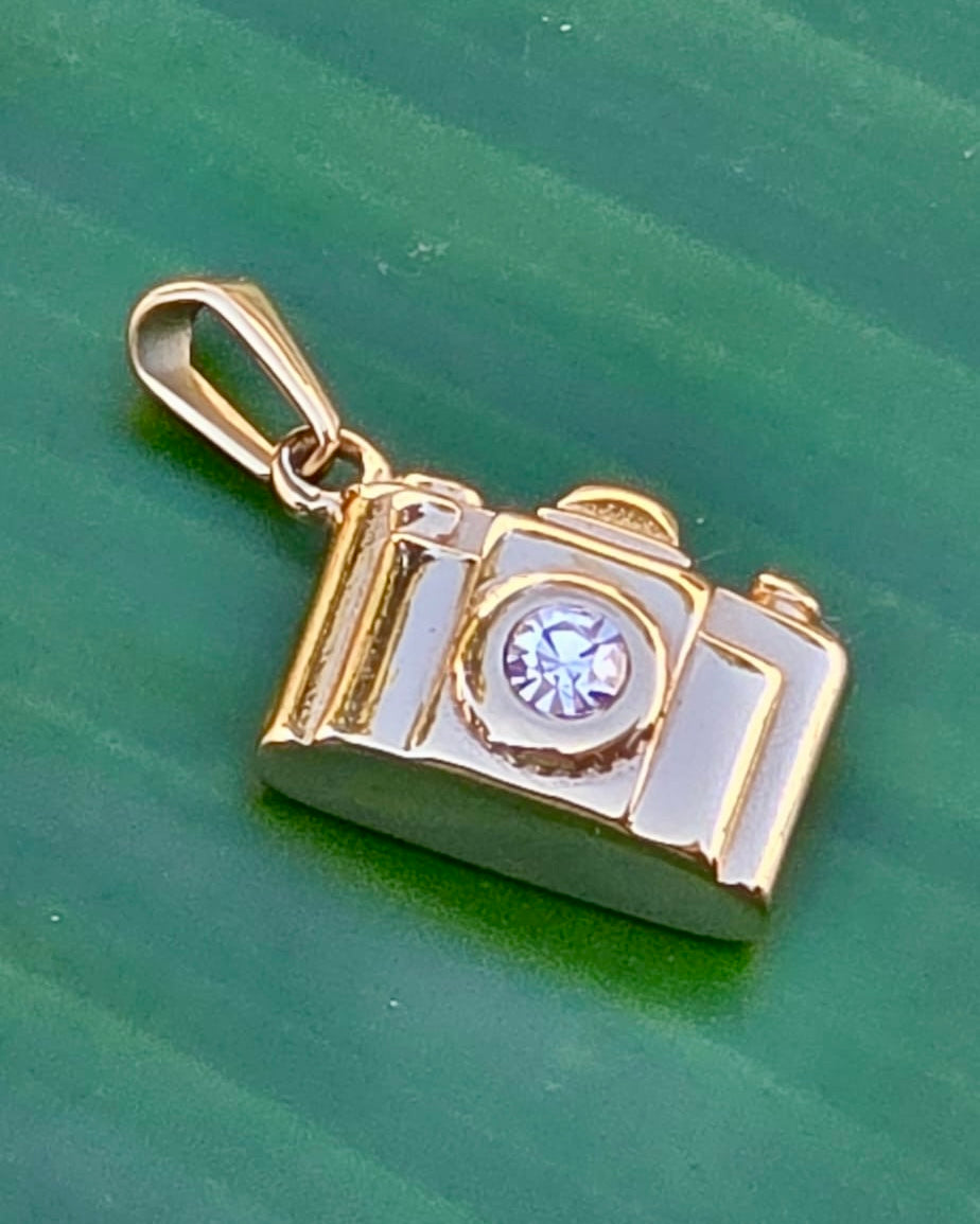 Gold stainless steel camera charm with a sparkling rhinestone lens, approximately one inch wide and bold in design.